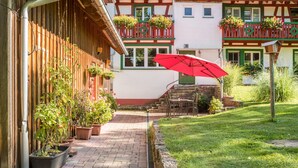 A courtyard with a red umbrella, potted plants, and a building with a balcony. - Holiday Apartment "Risthof 1" with Wi-Fi, Shared Garden, Sauna & Playground (Owingen)