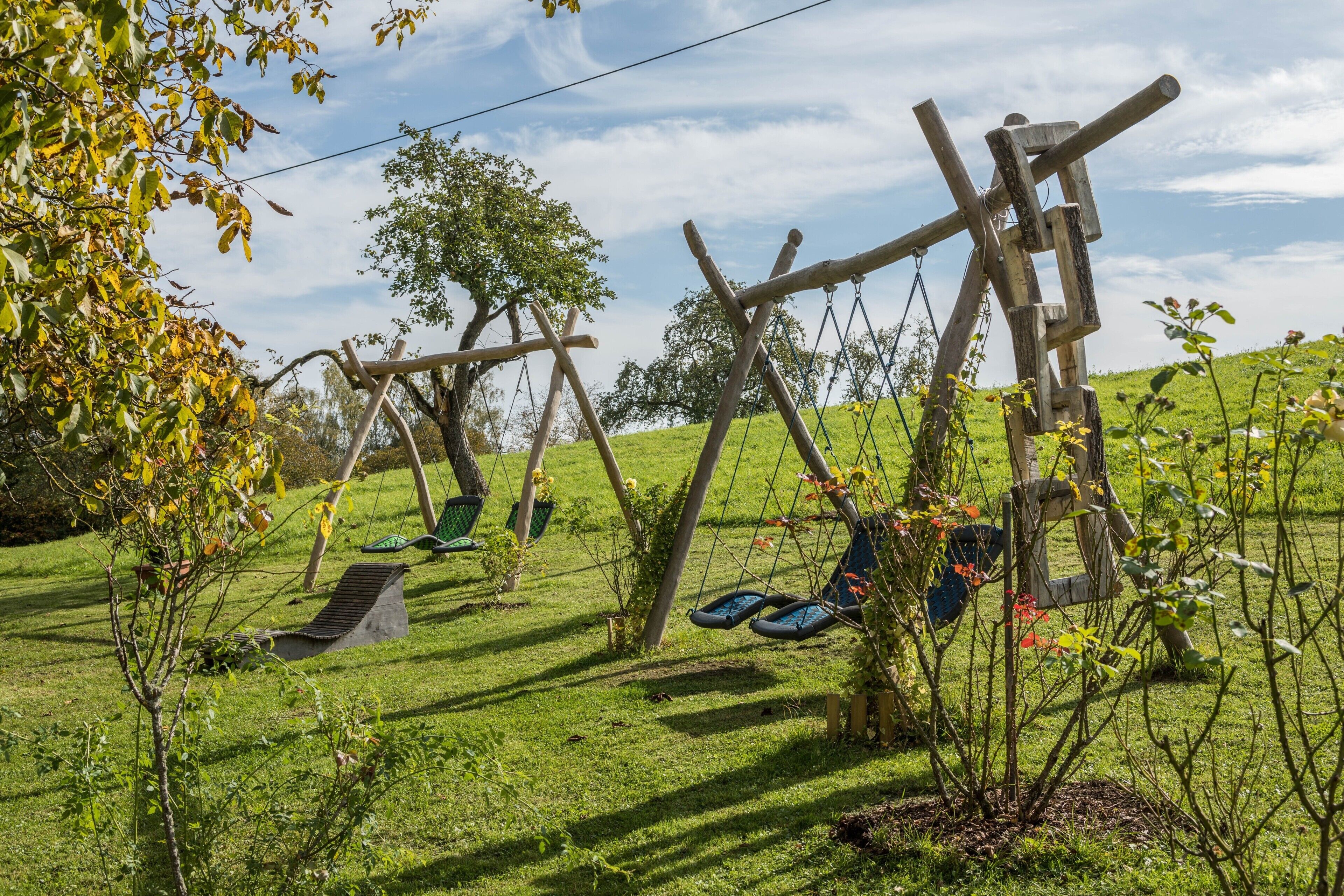Ein grünes Areal im Freien mit Holzschaukeln und einer kleinen Rutsche.