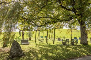 Um parque com baloiço, bancos e mesa para piquenique.