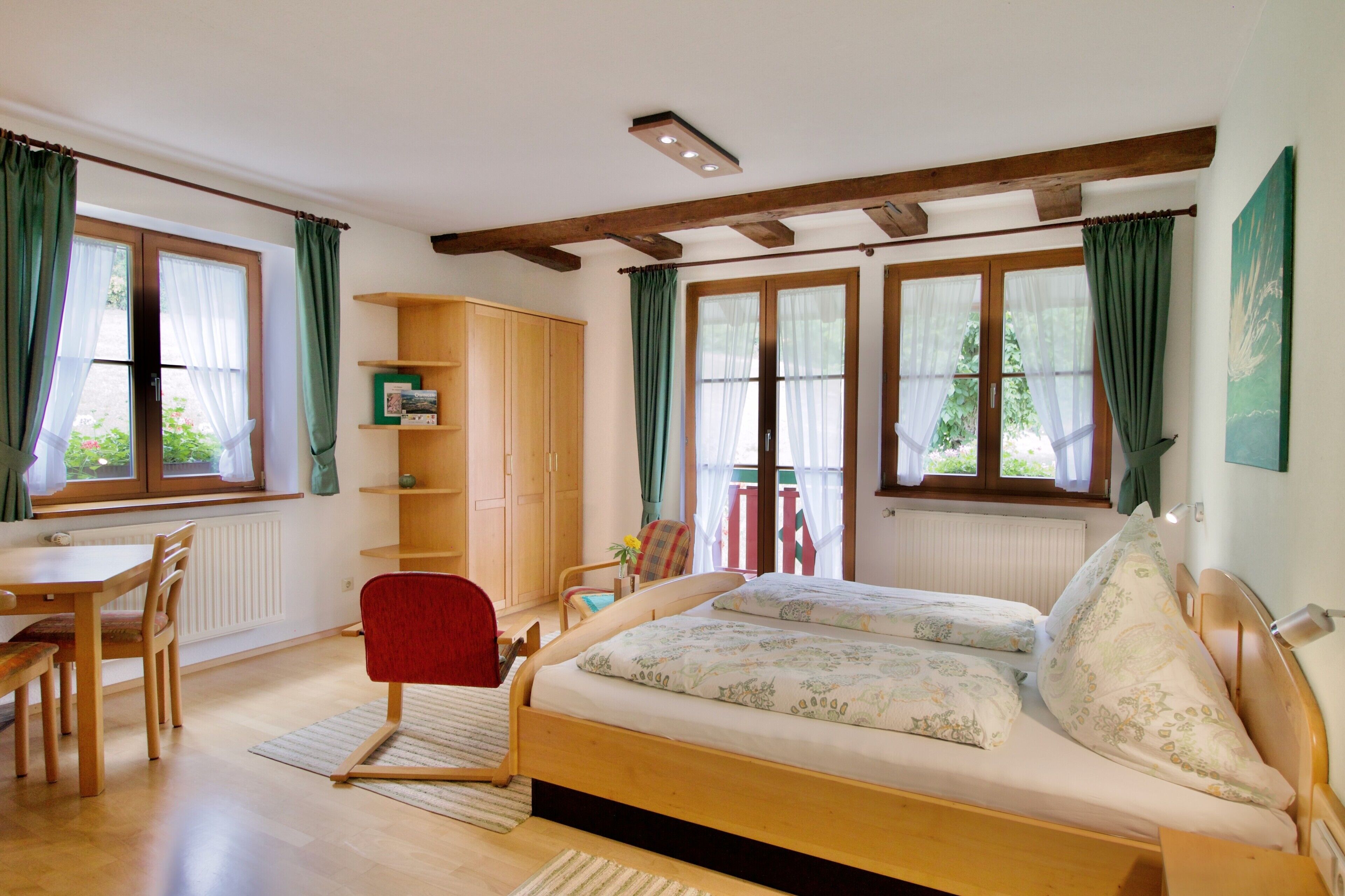 Una camera da letto con un letto, una scrivania, una sedia, un armadio e ampie finestre con tende.