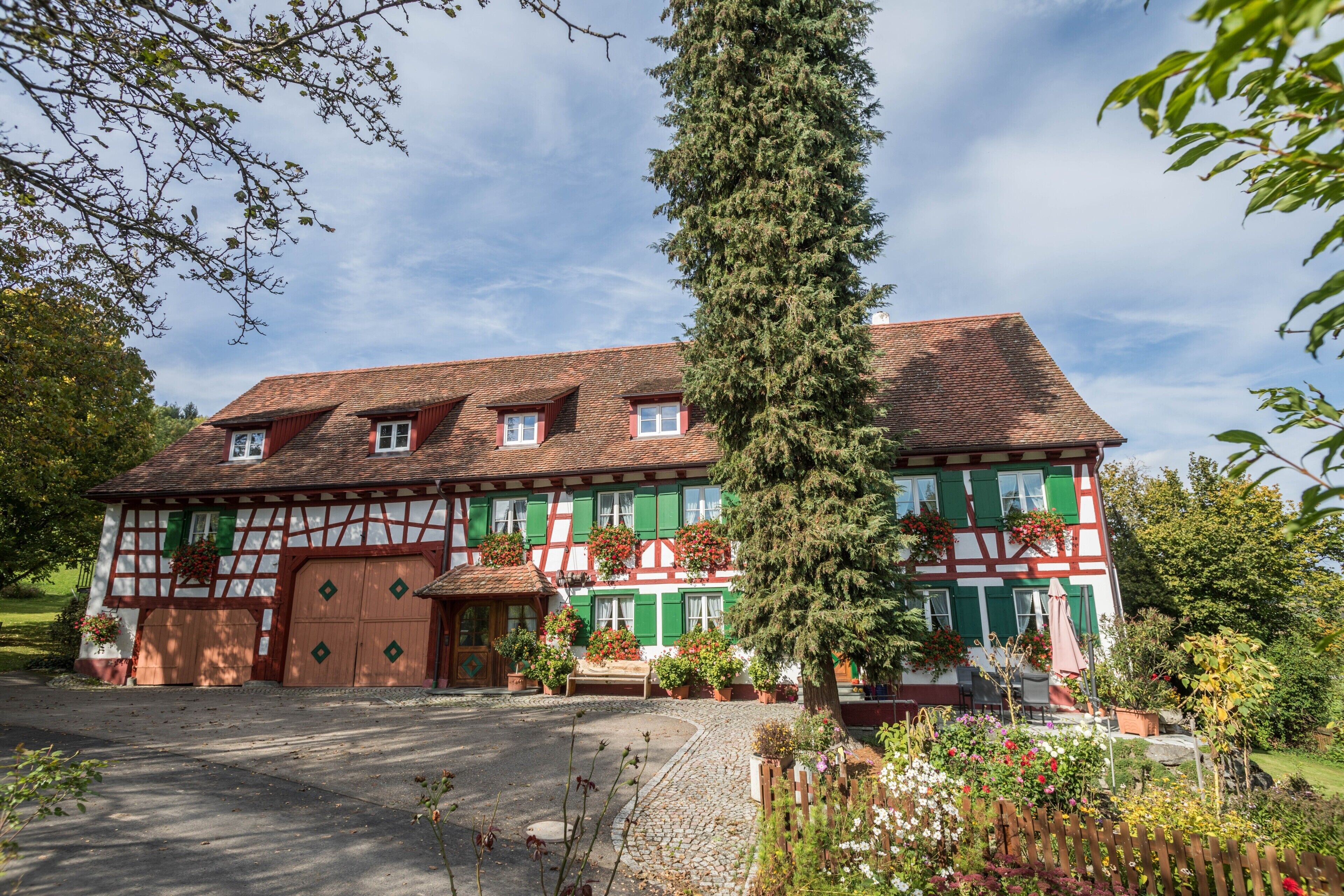 A traditional half-timbered house with a sloped roof, a wooden front door, and a garden with potted plants and flowers.