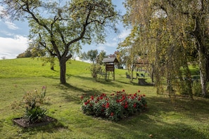 A grassy field with a wooden gazebo, a tree, and a small garden with red flowers. - Holiday Apartment "Risthof 2" with Shared Garden, Sauna and Playground (Owingen)