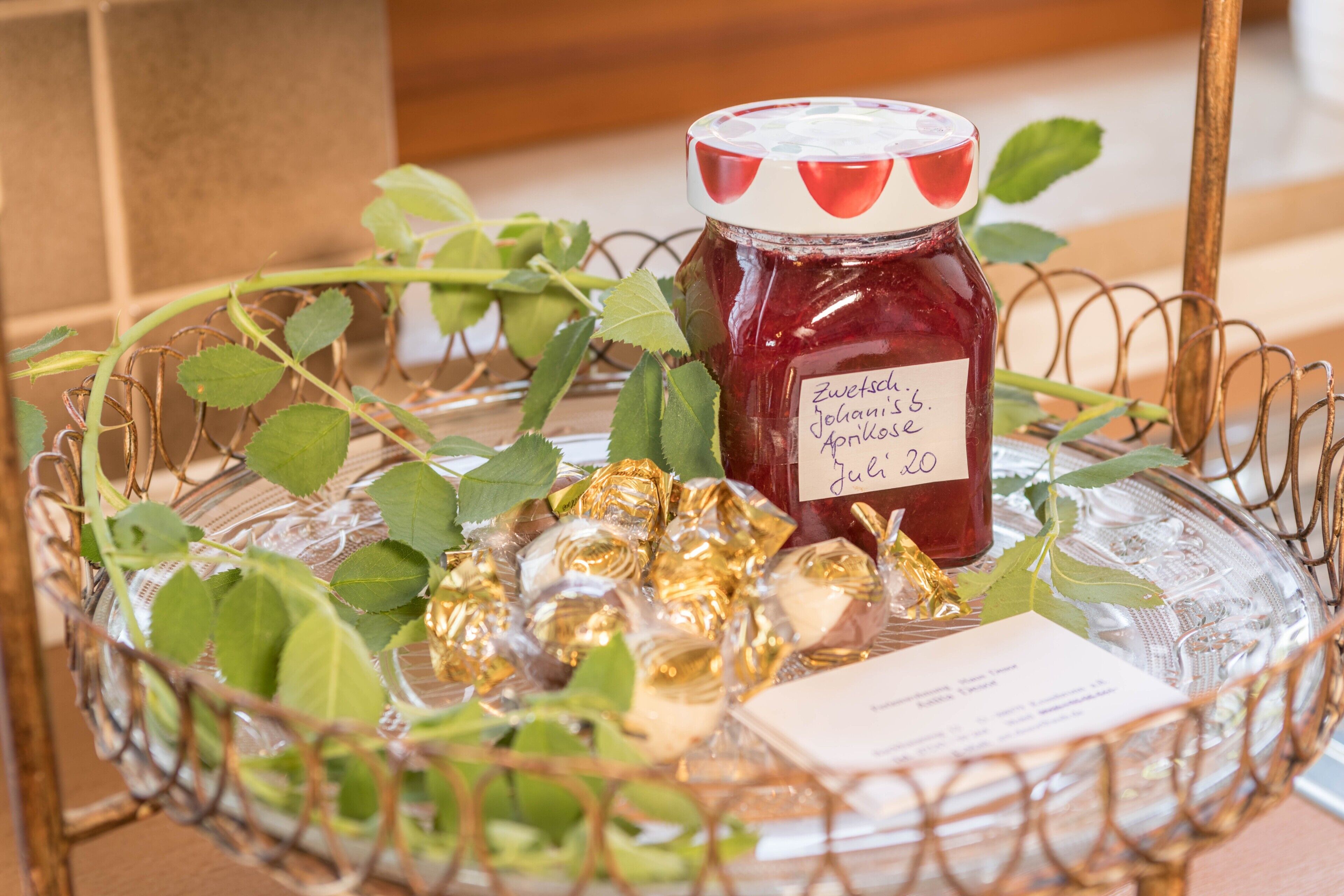 Ein Glasgefäß mit Marmeladenglas, verpackten Pralinen und einer Karte.