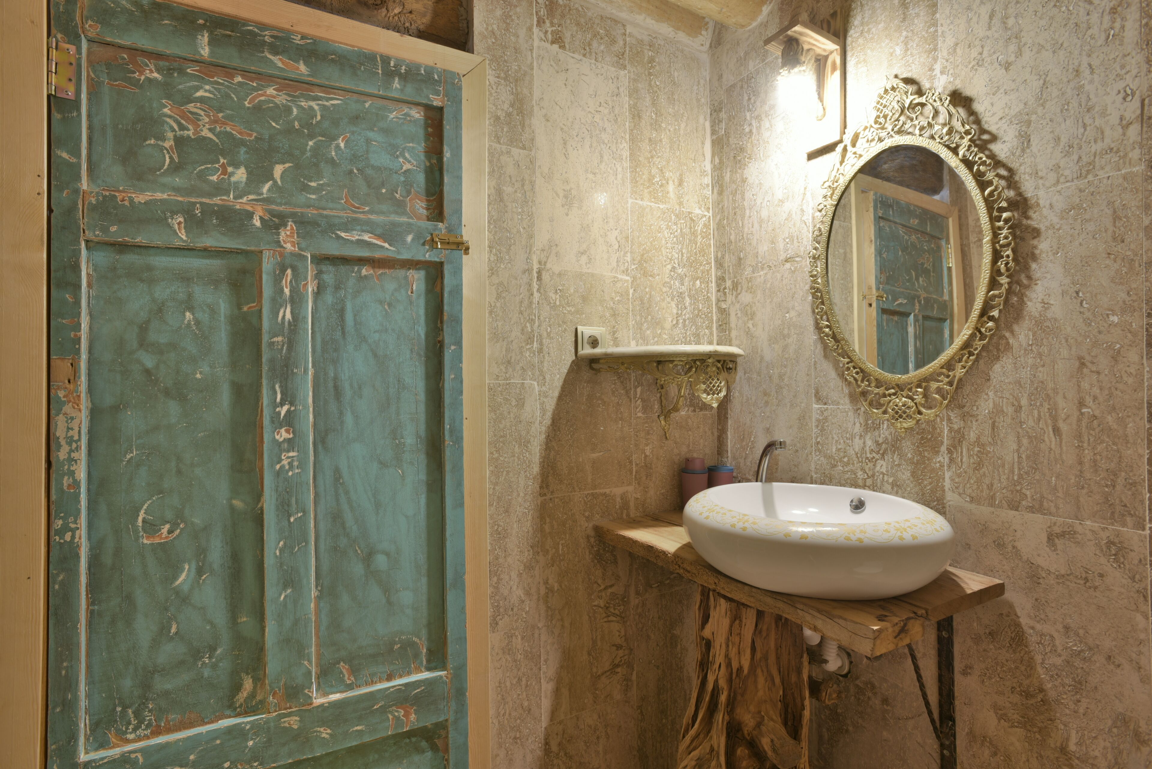 Un baño con una puerta rústica, un tocador de madera, un lavabo blanco y un espejo decorativo.