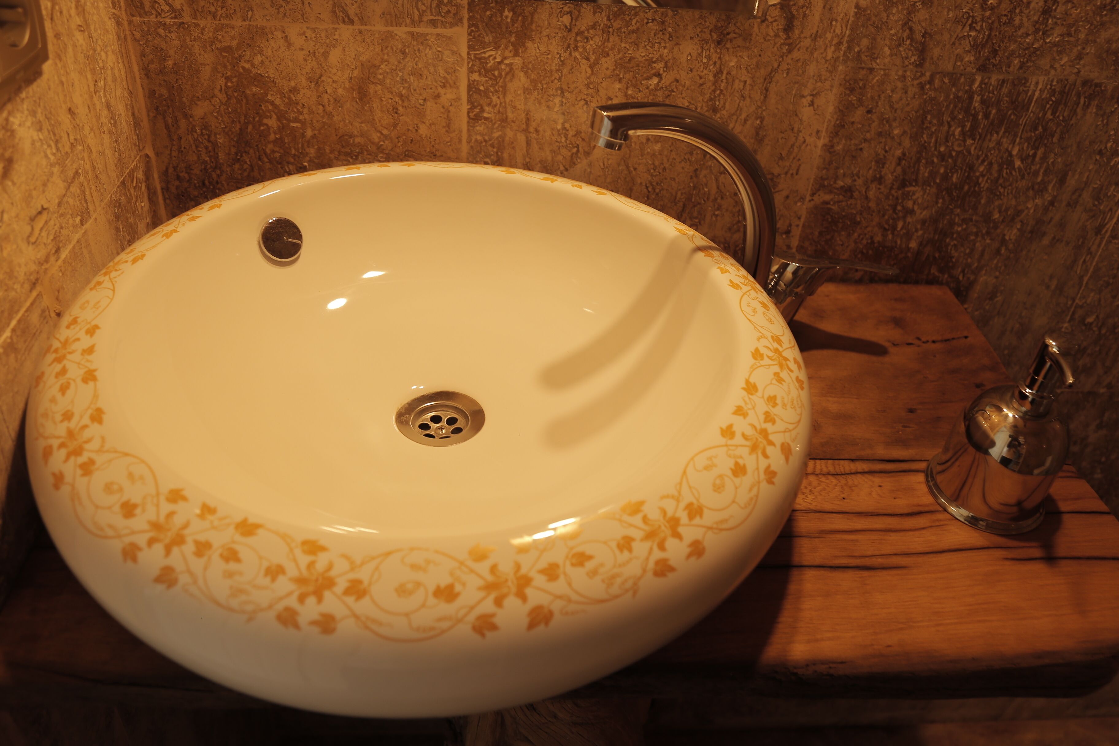 Ein Waschbecken mit Blumenmuster, einem Wasserhahn und einer Holzablage.
