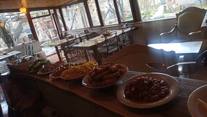 Um restaurante com interior em madeira, grandes janelas e diversos pratos expostos no balcão.