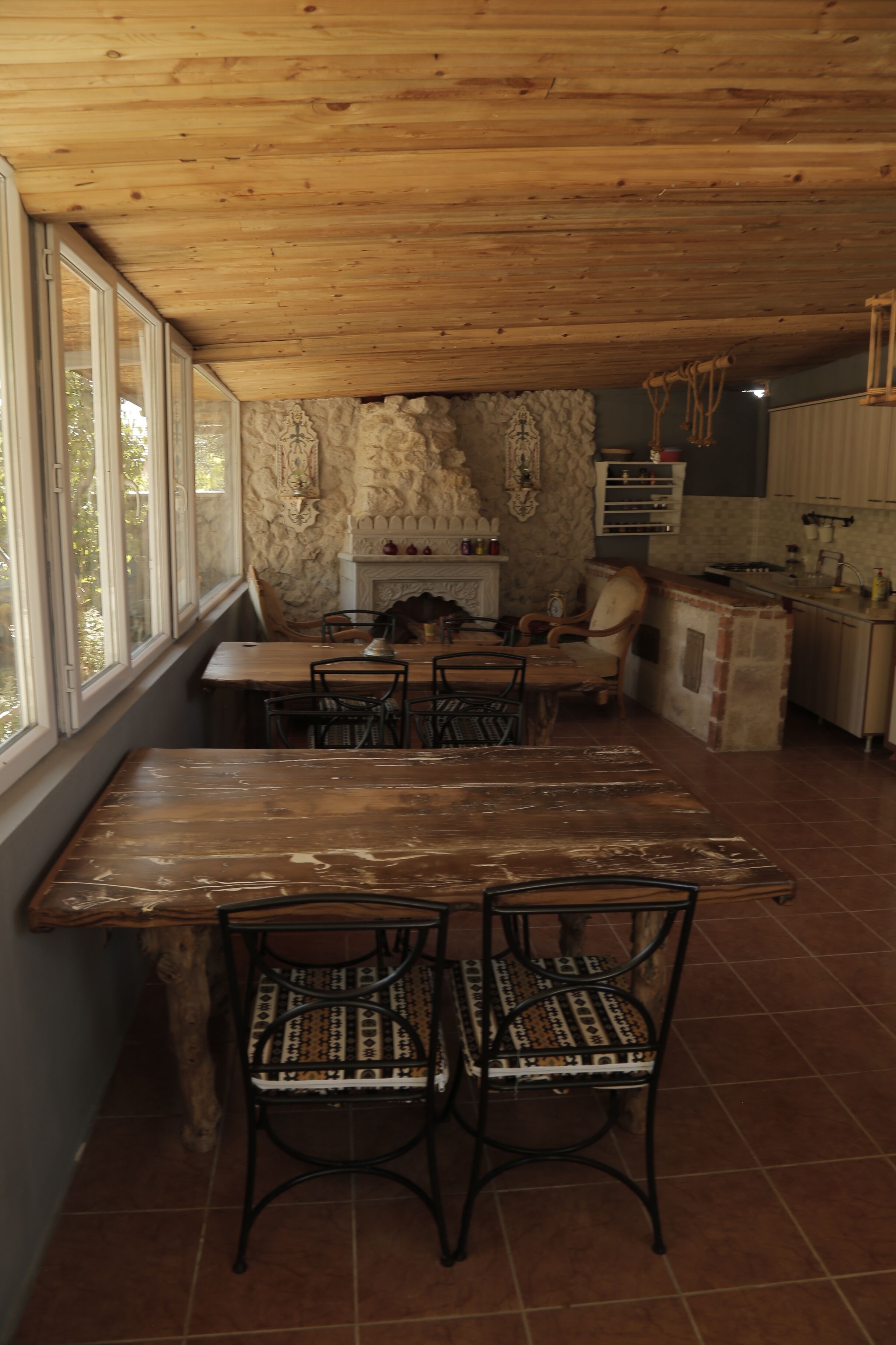A rustic dining area with a wooden table and chairs, a stone wall, and a kitchen area with cabinets and a countertop.