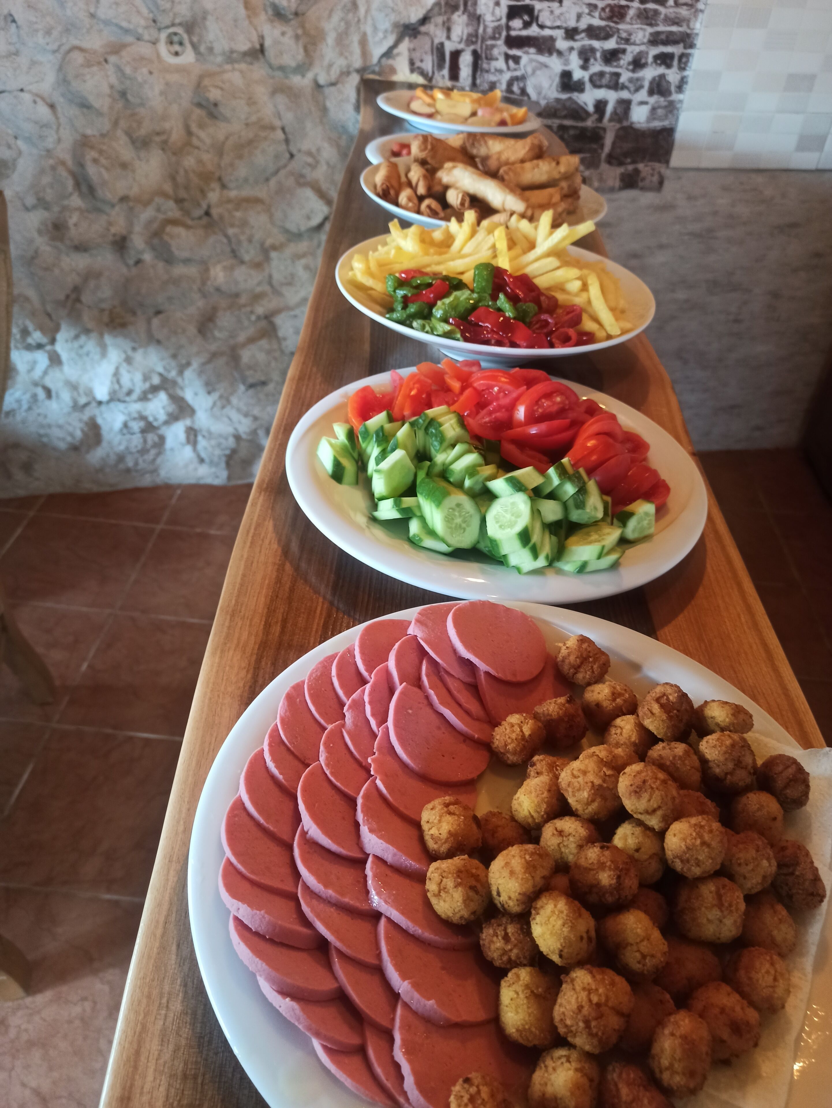 A table with various dishes including sliced meat, tater tots, and a salad.