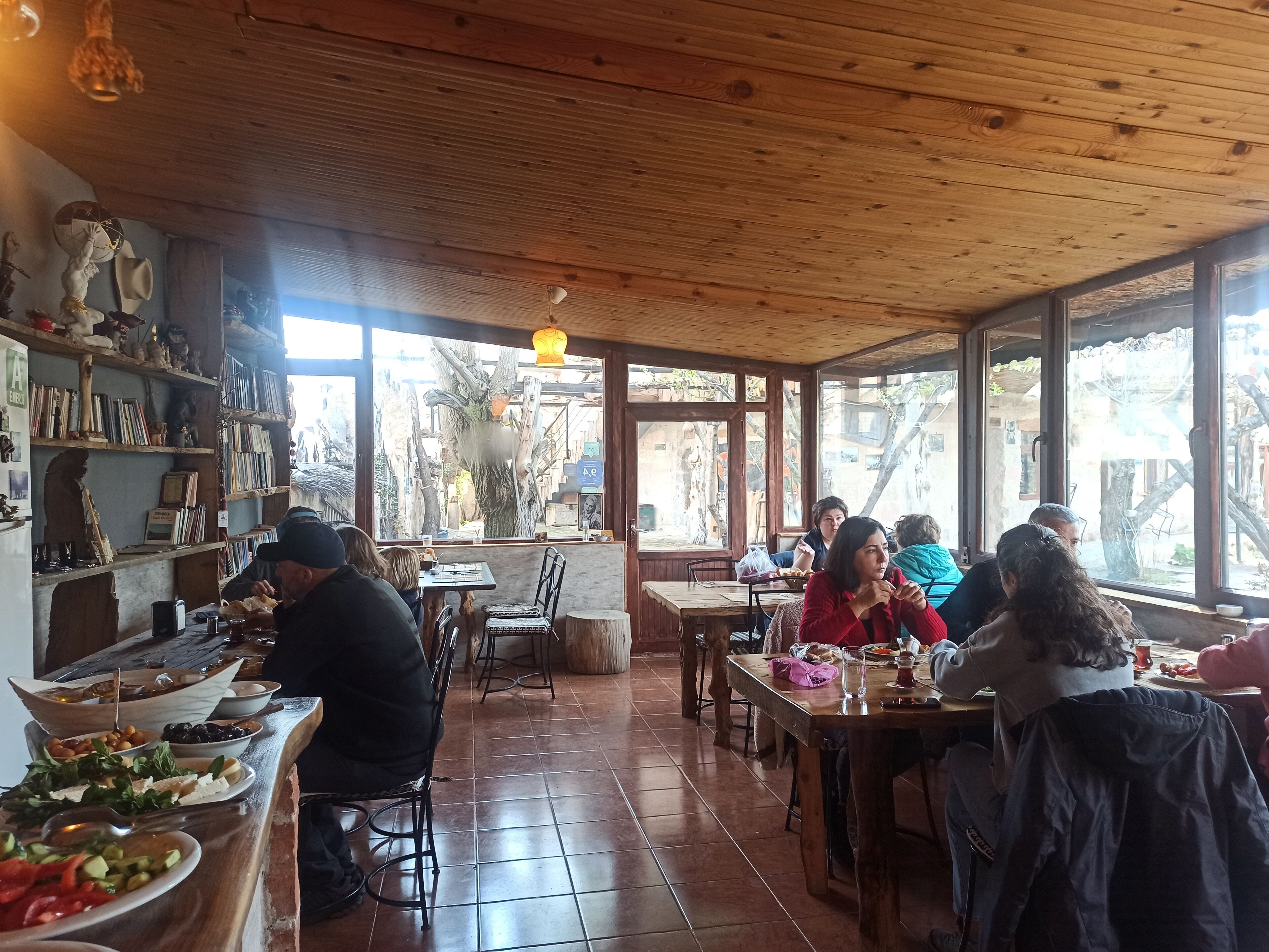 Un interior rústico de madera con una zona de comedor, estanterías llenas de libros y objetos decorativos, y vistas al exterior.