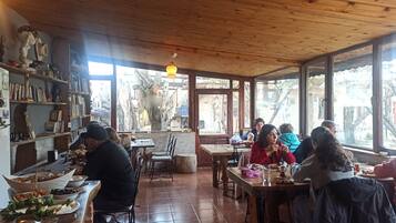 Un interior rústico de madera con una zona de comedor, estanterías llenas de libros y objetos decorativos, y vistas al exterior.