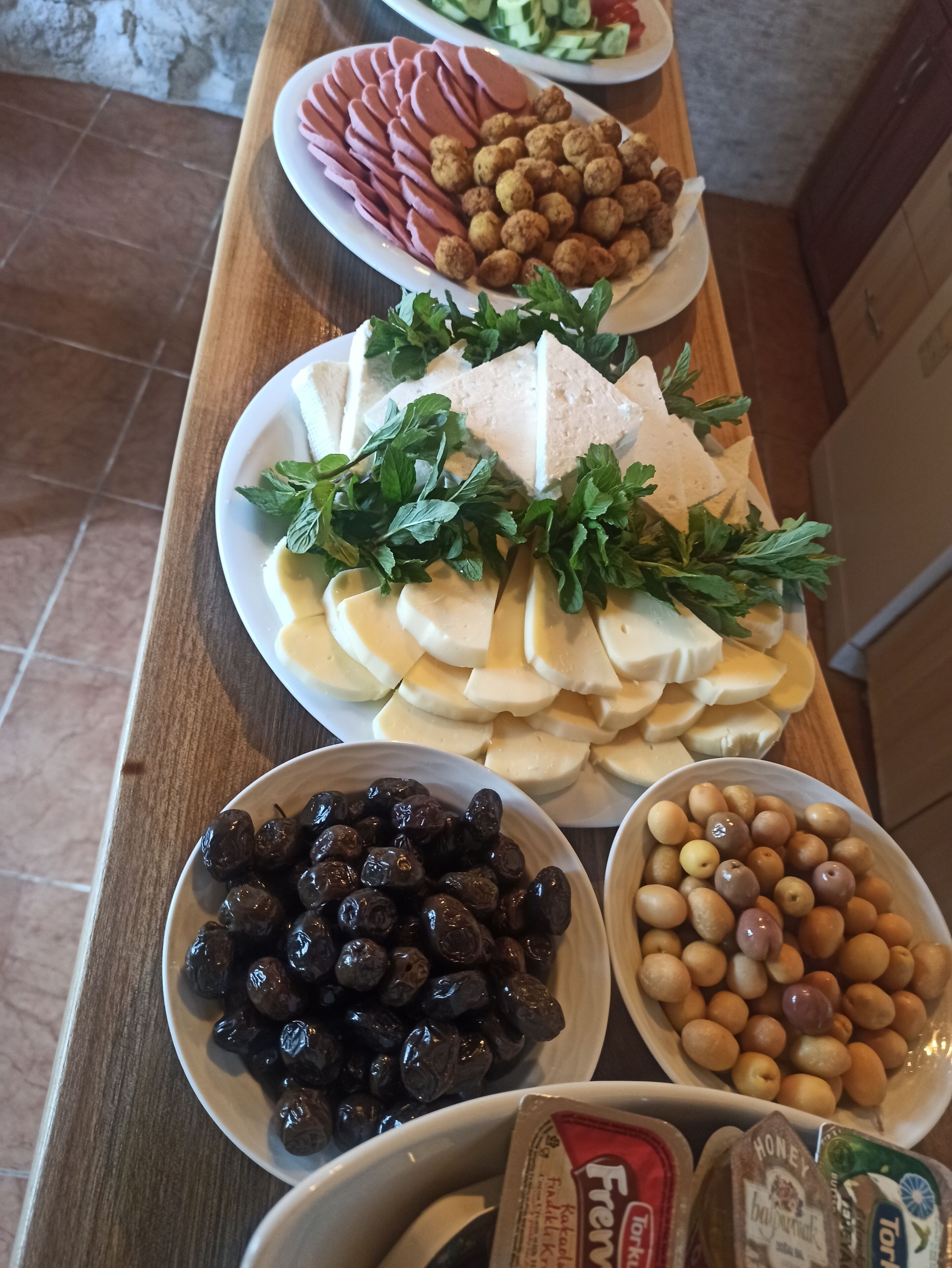 Uma mesa de buffet com diversos alimentos, incluindo carnes fatiadas, queijos, azeitonas e nozes.