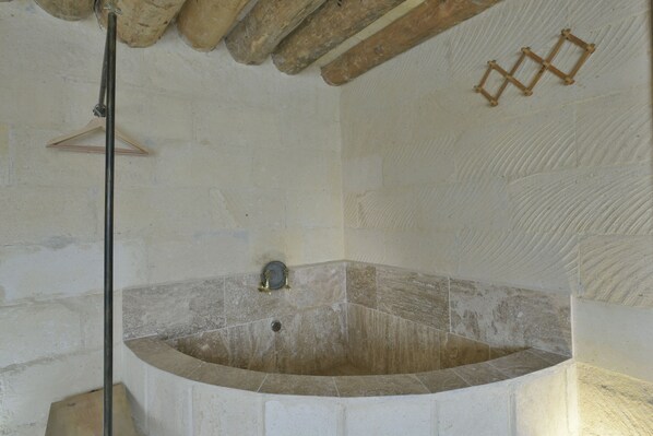 A stone bathtub with a wooden ladder, a towel rack, and a stone wall.
