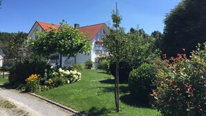 A residential area with a house featuring a red-tiled roof, surrounded by lush greenery and a well-maintained lawn.