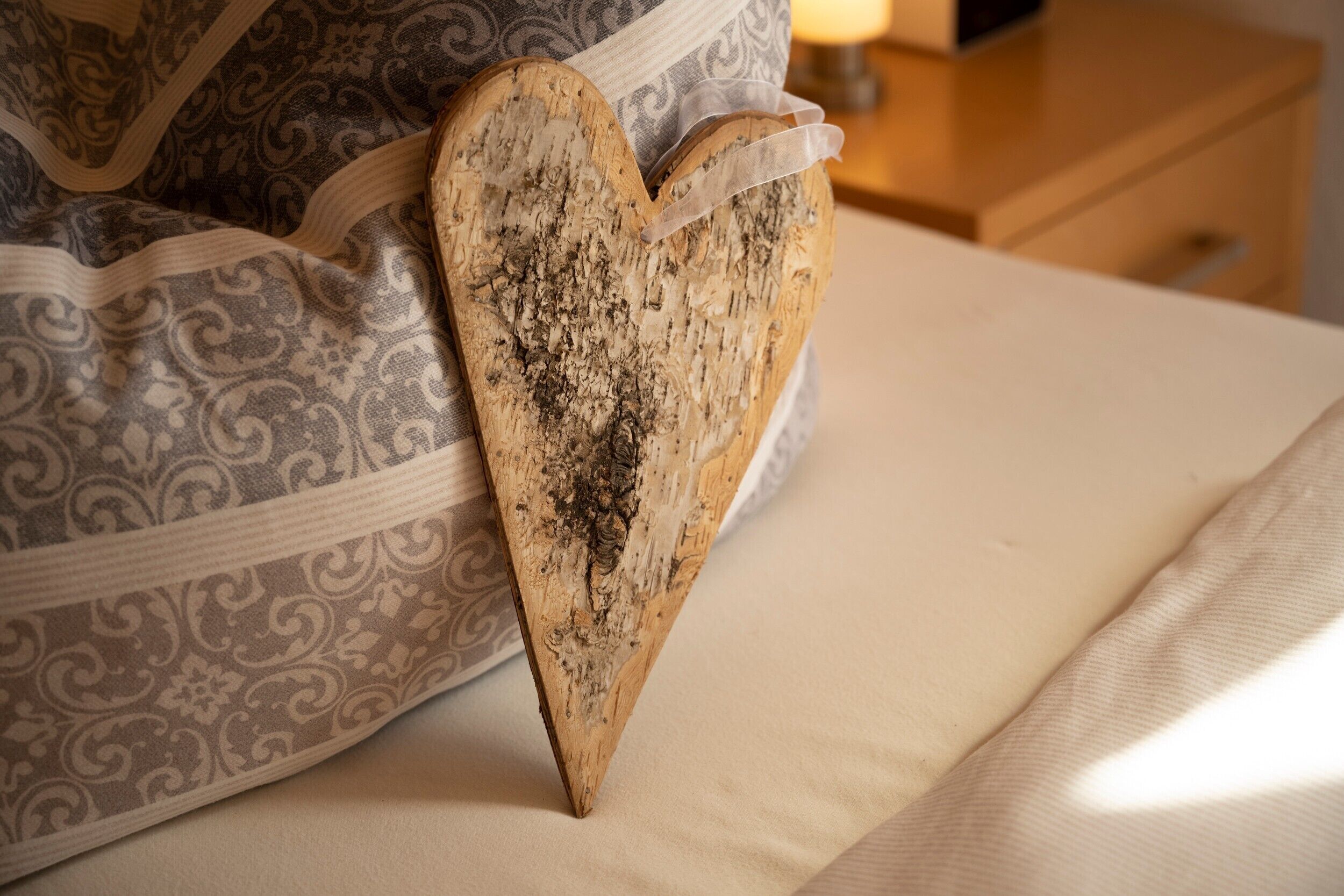 Een bed met een gekleurd kussen en een houten hartvormig object.