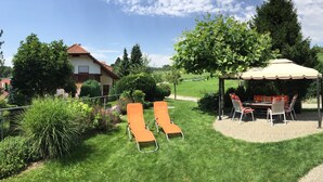 A garden with a gazebo, two lounge chairs, and a dining table.