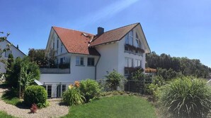 A two-story house with a red-tiled roof, a front garden, and a clear blue sky.
