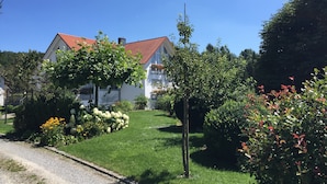 Ein Wohngebiet mit einem Haus mit rotem Ziegeldach, umgeben von üppiger Vegetation und einem gepflegten Rasen.