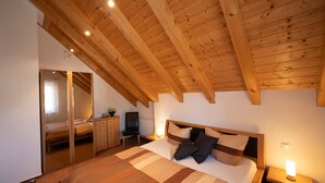 Quarto com teto de madeira, cama com roupa de cama listrada, mesa de cabeceira com abajur e espelho.