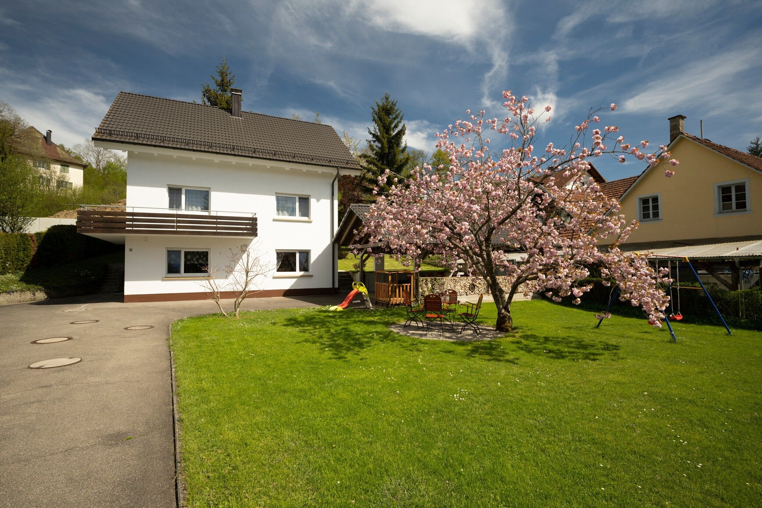 A two-story house with a white exterior, a brown roof, and a front yard with a cherry blossom tree.