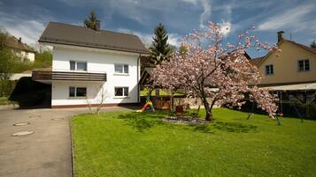 A two-story house with a white exterior, a brown roof, and a front yard with a cherry blossom tree.