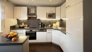 Uma cozinha moderna com armários brancos, eletrodomésticos de aço inoxidável e bancada escura.