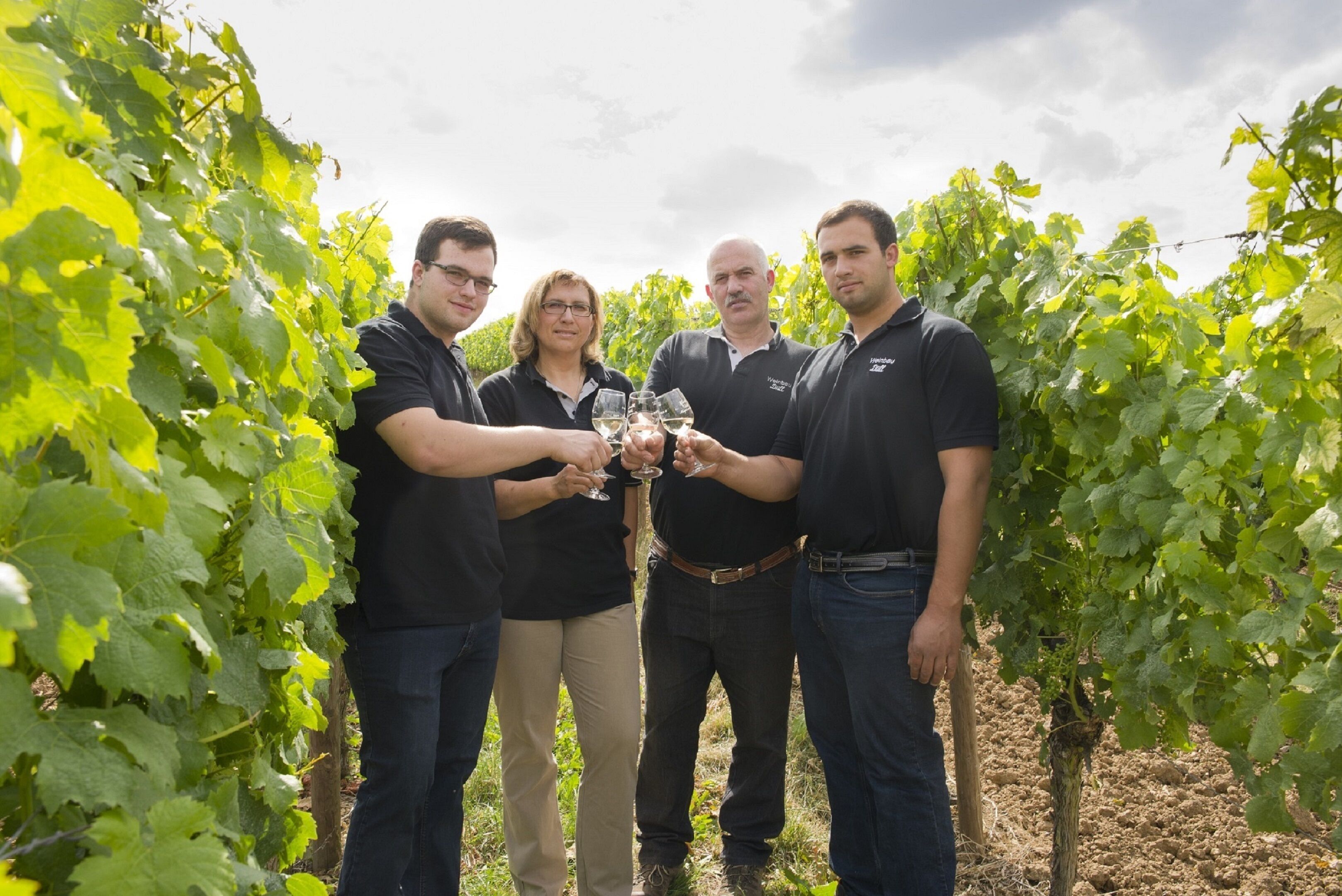A group of people in a vineyard holding wine glasses.