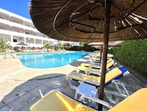 A poolside area with lounge chairs and umbrellas, a clear blue pool, and a building in the background. - Alvaflor - Vilamoura (Vilamoura)