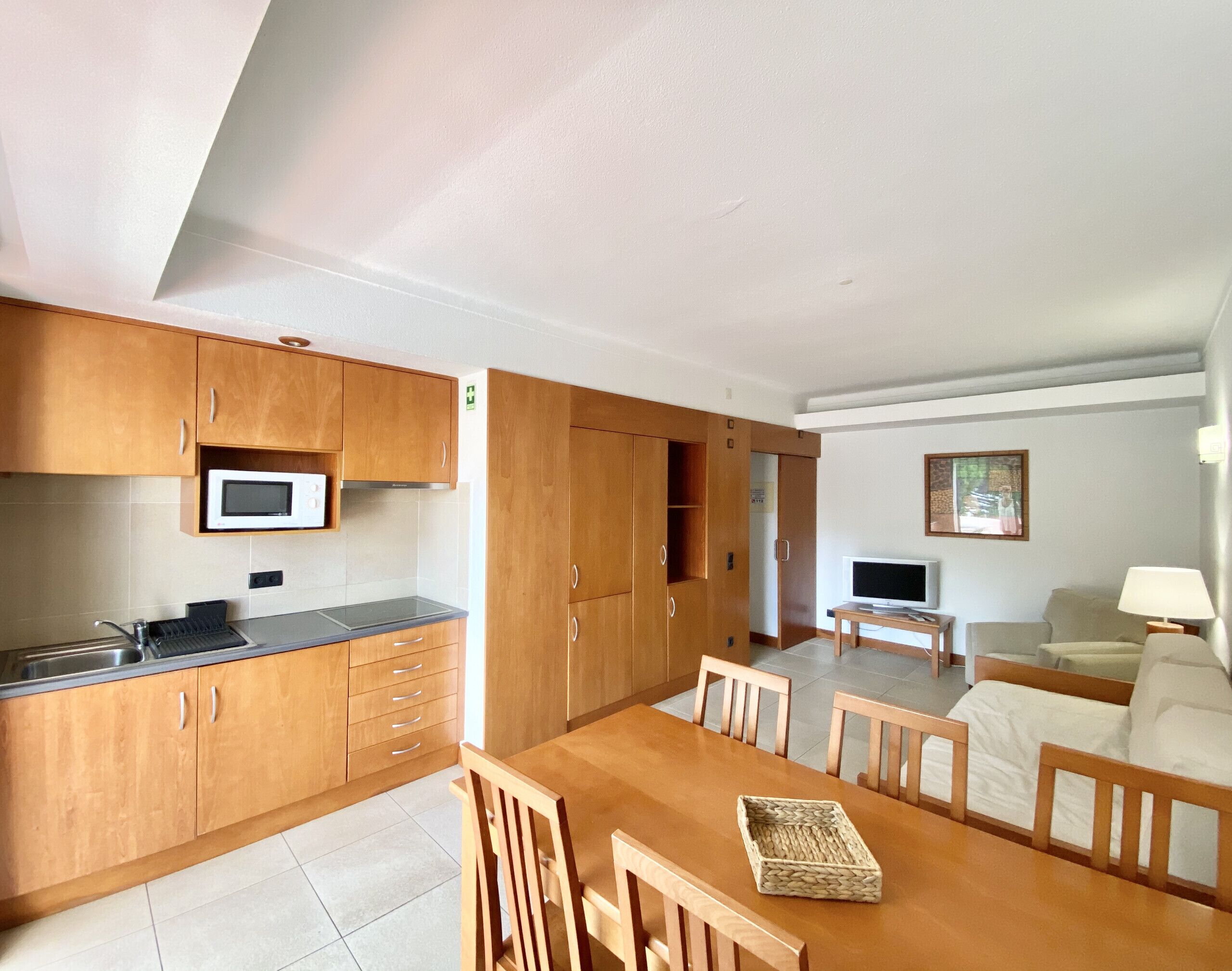 A compact kitchen with wooden cabinets, a microwave, and a dining area with a table and chairs.