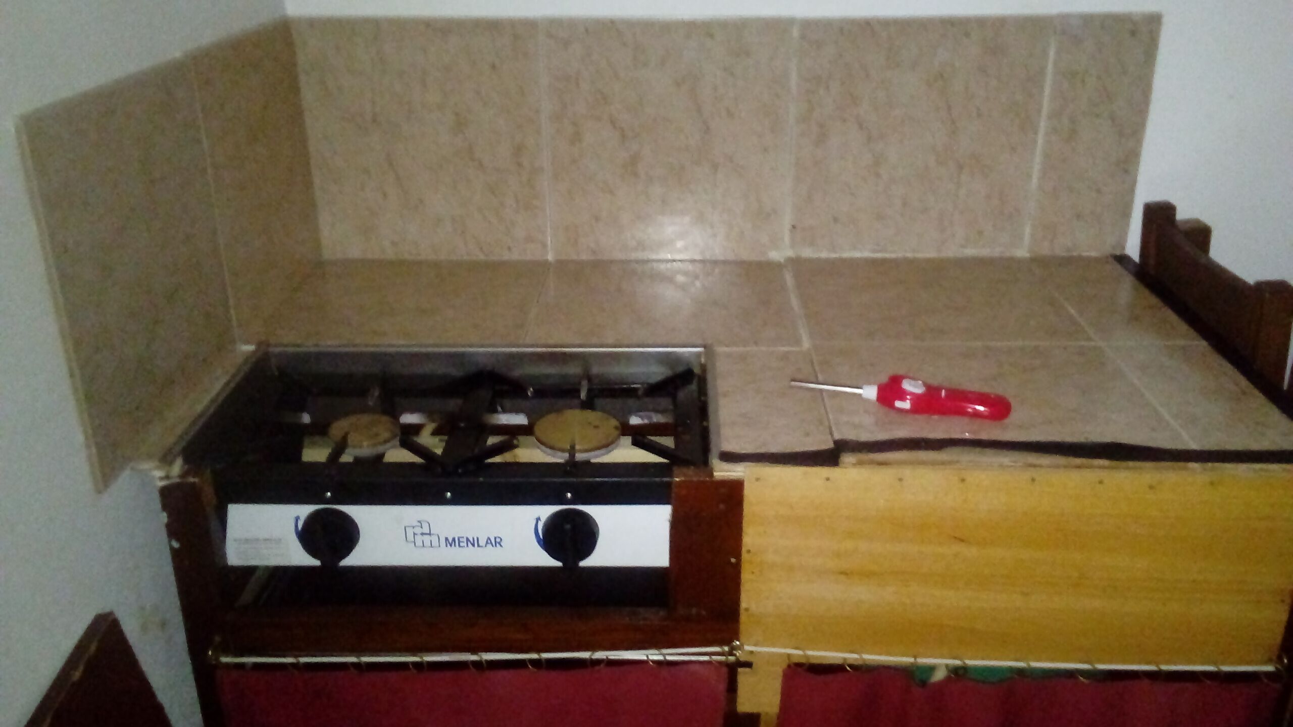 Una cocina con estufa a gas, un destornillador rojo sobre la encimera y una cortina roja.