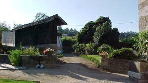 Un edificio rústico con techo inclinado, rodeado de vegetación y un sendero de adoquines.