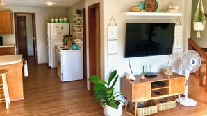 A modern kitchen with white appliances, a dining area with a wooden table, and a living space with a TV and fan. - The Shell Shack-Darling and peaceful cottage (Pacific City)