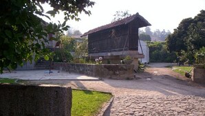 Ein rustikales Gebäude mit geneigtem Dach, umgeben von einem Steinweg und Grünpflanzen.