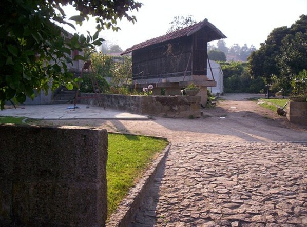 Un edificio rústico con techo inclinado, rodeado por un sendero de piedra y follaje.