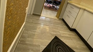 Un couloir étroit avec un mur orné de motifs, un tapis noir à motifs circulaires et une vue sur un coin repas avec une table et des chaises.