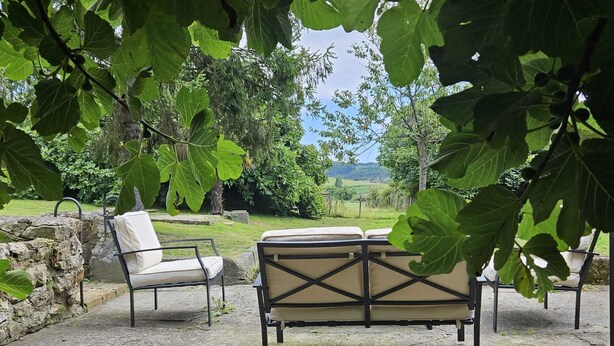 An outdoor seating area with two chairs and a table, surrounded by large green leaves and a stone wall. - House in Galizano with garden (Cantabria)
