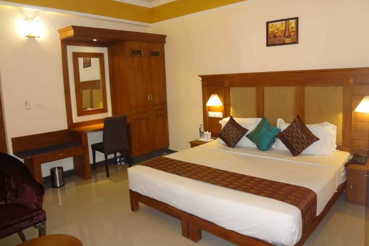 A hotel room with a large bed, a desk, a chair, and a wardrobe.