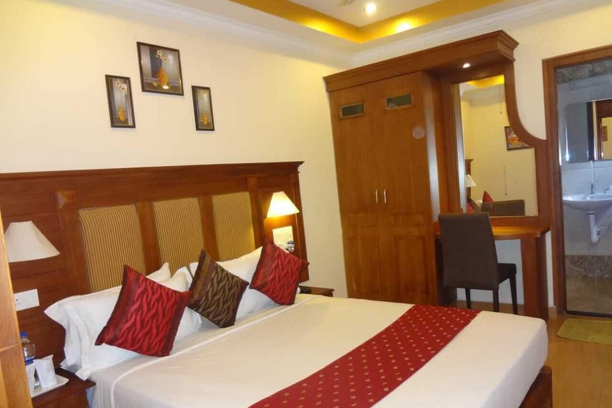A hotel room with a large bed, wooden headboard, a desk with a chair, and a bathroom visible through a glass door.