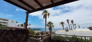 A coastal hotel with a stone wall, palm trees, and a view of the sea.