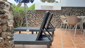 Une terrasse avec des meubles d’extérieur, un mur en pierre et un sol carrelé.