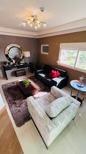 A modern living room with a sofa, a coffee table, a side table, a mirror, a lamp, and a window with a view.