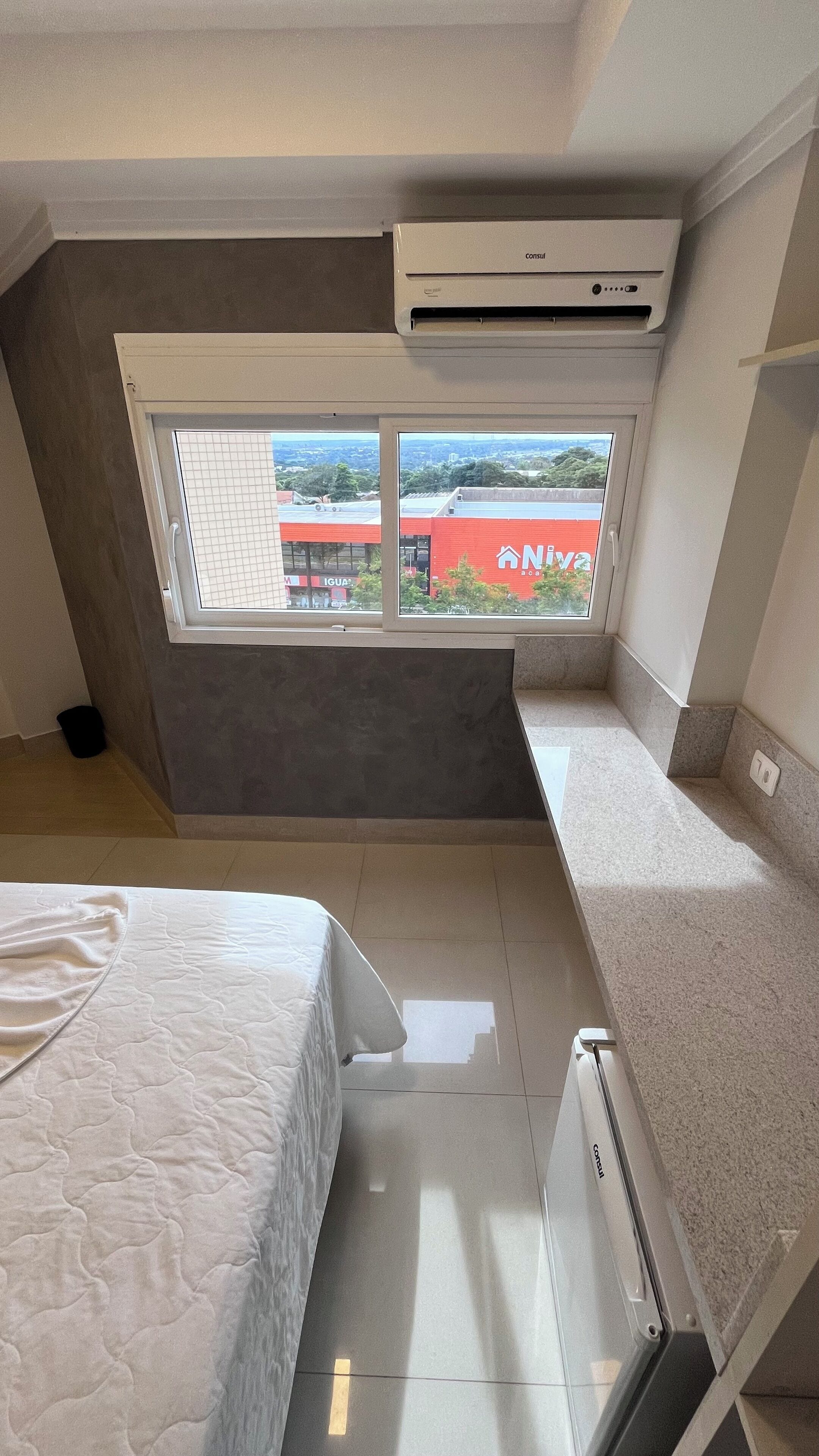 A small, modern room with a bed, a desk, and a window overlooking a cityscape.