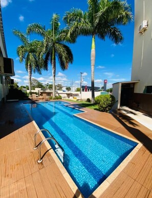 A swimming pool with a wooden deck, surrounded by palm trees and a clear blue sky.