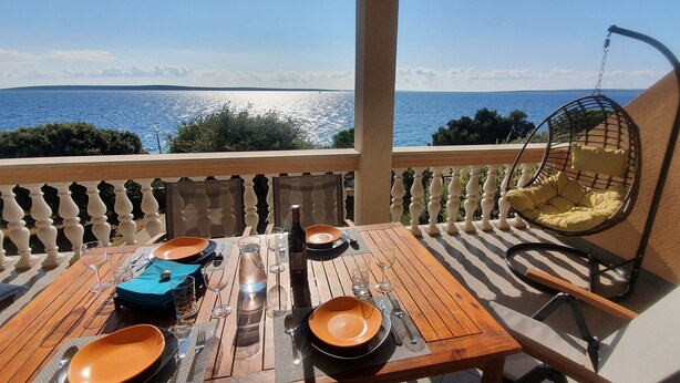 A wooden table set for a meal with a hanging chair and a view of the sea. - Beach front apartment for family vacation in Mandre (Mandre)