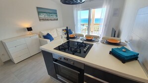 A modern kitchen with a central island, a dining area with a view of the sea, and a white sofa with blue cushions. - Beach front apartment for family vacation in Mandre (Mandre)