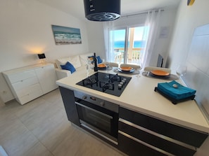 Una cucina moderna con isola centrale, zona pranzo con vista mare e un divano bianco con cuscini blu.