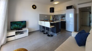 A modern kitchen with white cabinets, a built-in oven, and a dining area with a white table and bar stools. - Beach front apartment for family vacation in Mandre (Mandre)