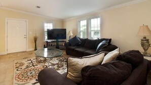 A living room with a sofa, a coffee table, a TV, and a lamp. - Gardens, St. Mary's, JFK, Good Samaritan, VA (West Palm Beach)