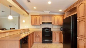 A kitchen with wooden cabinets, a black refrigerator, a stove, and a dishwasher. - Gardens, St. Mary's, JFK, Good Samaritan, VA (West Palm Beach)