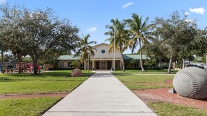 A building labeled "Man Park Community Center" with a central pathway leading to it, surrounded by grass and palm trees. - Gardens, St. Mary's, JFK, Good Samaritan, VA (West Palm Beach)