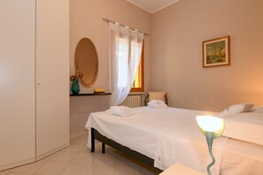 A bedroom with a bed, a bedside lamp, a window with curtains, a radiator, a mirror, and a framed picture on the wall. - Garden Residence Malcesine Lake View  App. G1 (Malcesine)